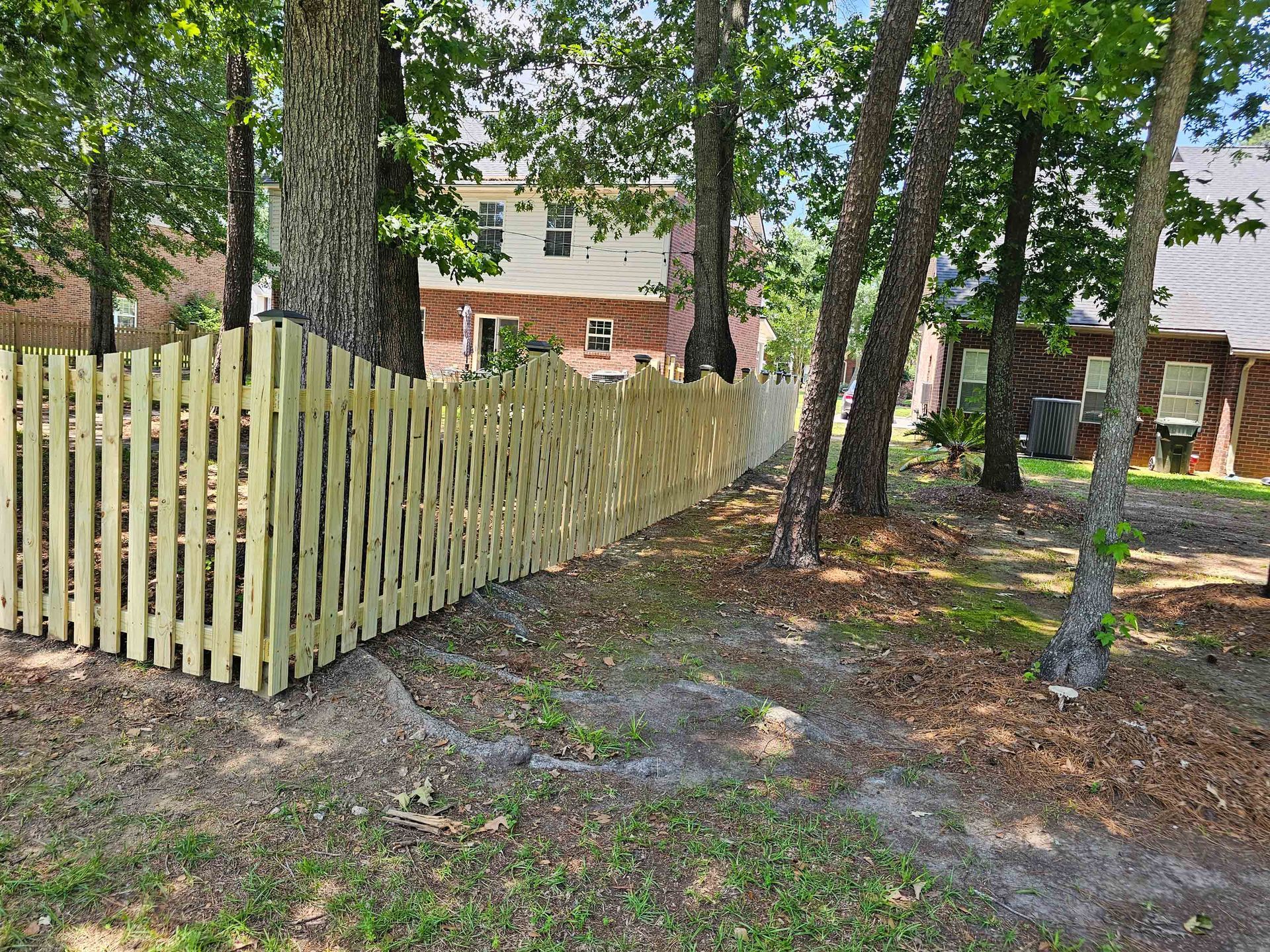 A newly built wooden picket fence in a backyard, partially shaded by trees.