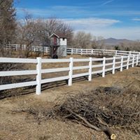 White ranch fence, small wooden structure, and dry brush against a blue sky.