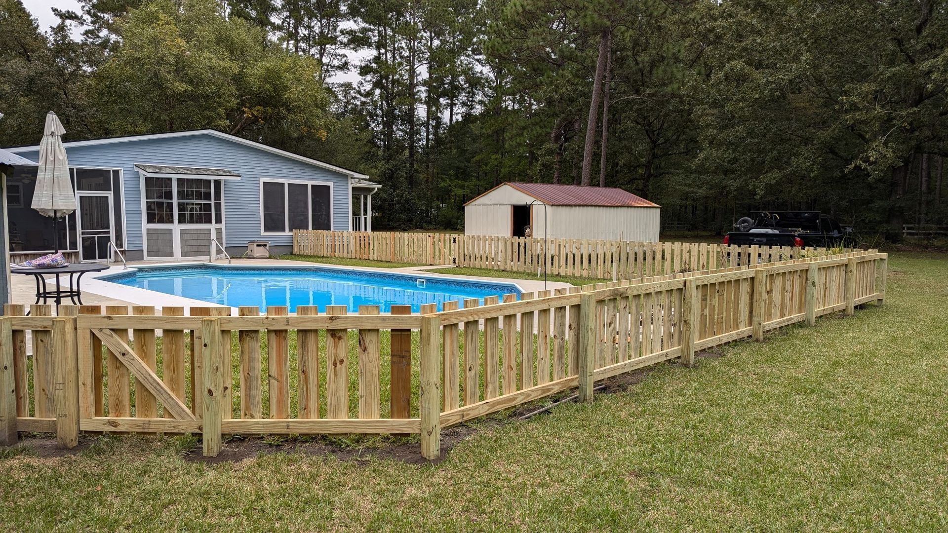 Wooden fence surrounds a backyard swimming pool and a small shed.
