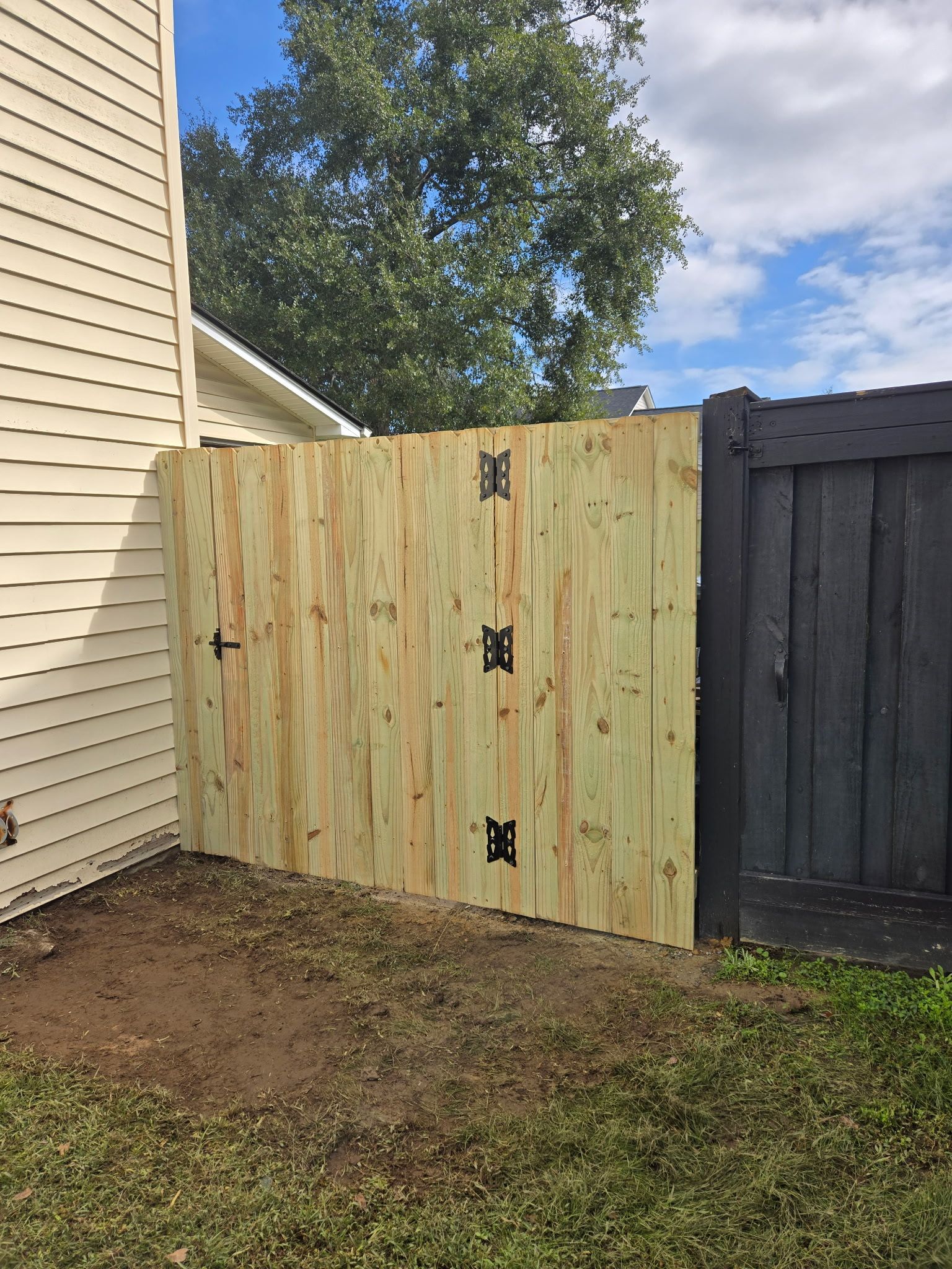 Wooden gate in a backyard, attached to a house and a black fence.