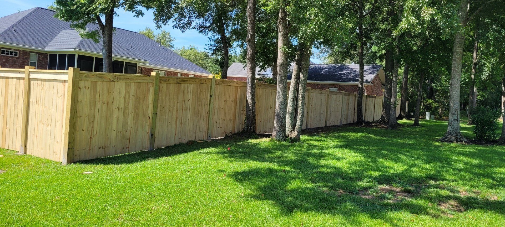 Wooden fence in a grassy yard, trees in the background, blue sky.