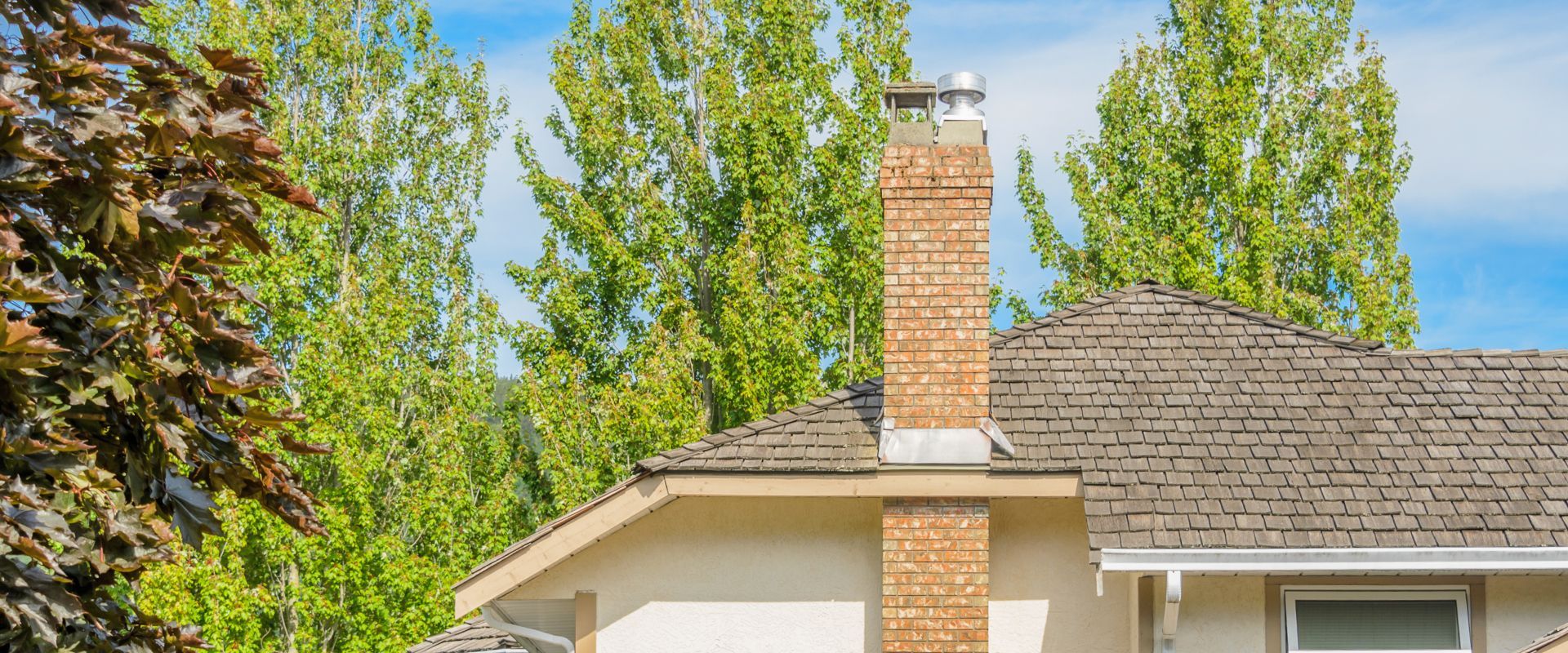 Brick chimney on a suburban house roof with green trees in the background