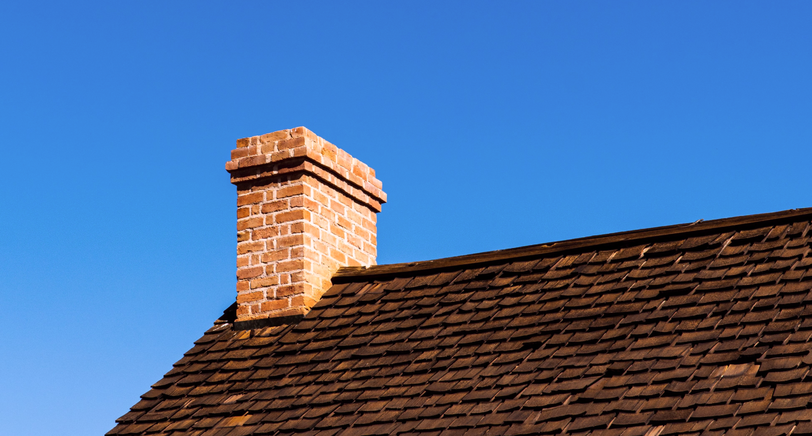 Brick chimney on a shingled roof against a clear blue sky