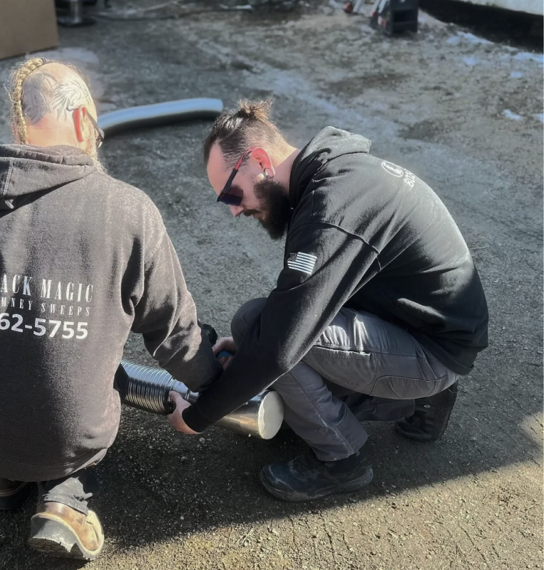 Two workers crouch on pavement, using a hose or tool near a wet area outside.