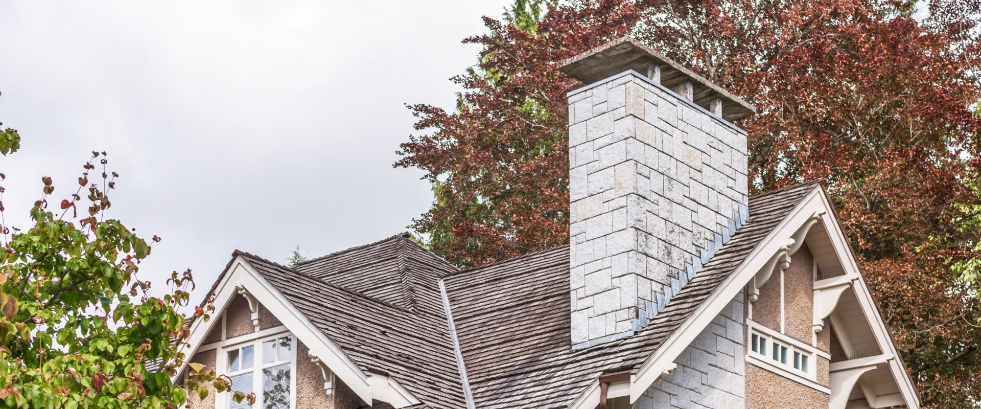 House roof with a white brick chimney beside a large tree with red autumn leaves