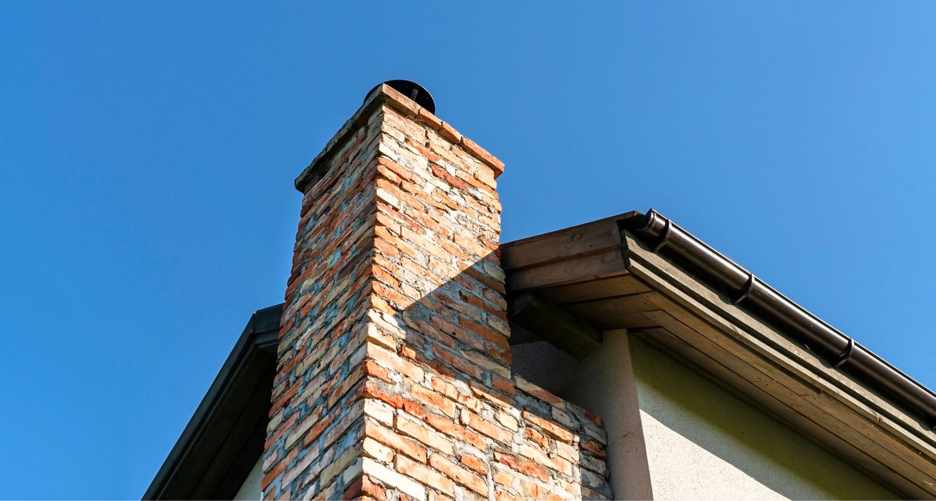 Brick chimney beside a house roof against a clear blue sky