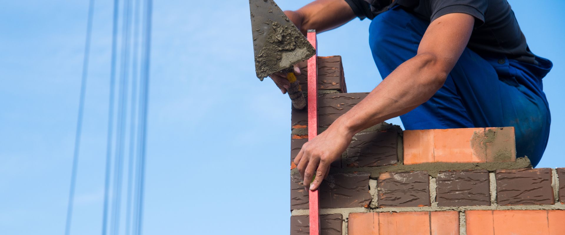 Bricklayer placing bricks on a wall at a construction site against a blue sky