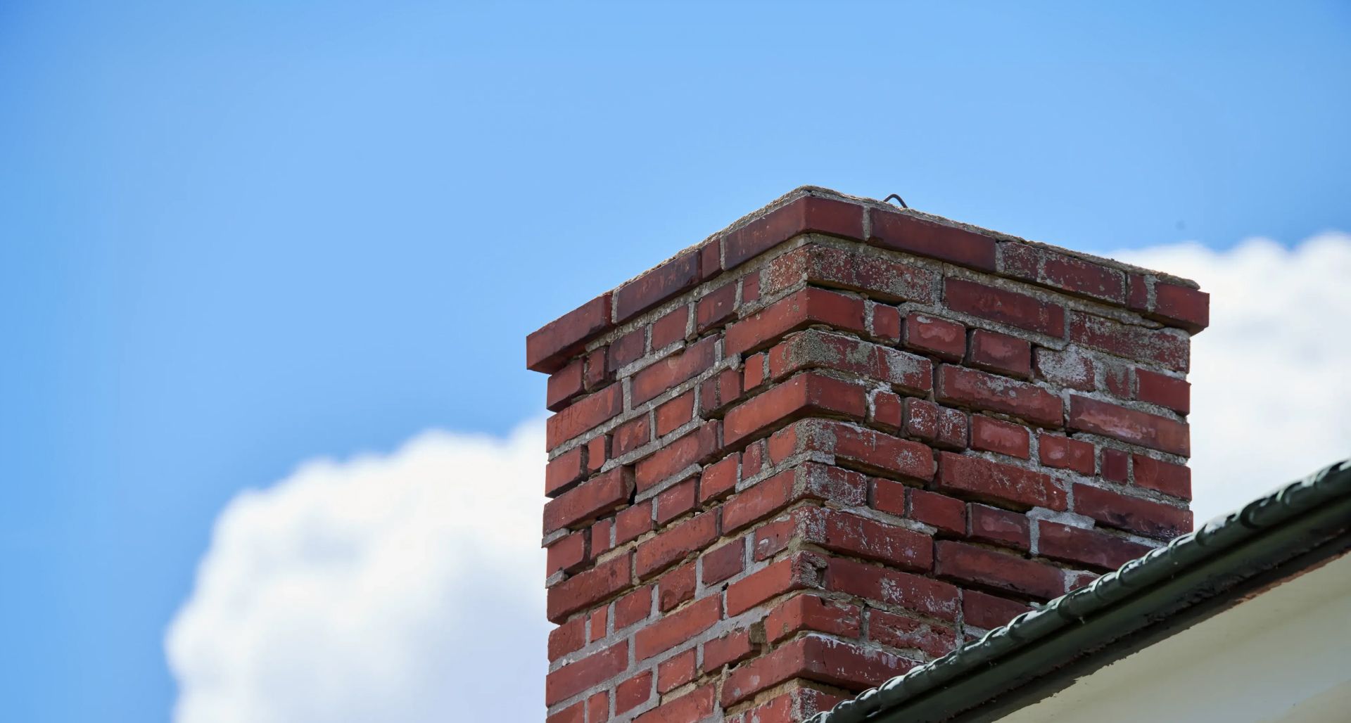 Red brick chimney against a blue sky with a white cloud