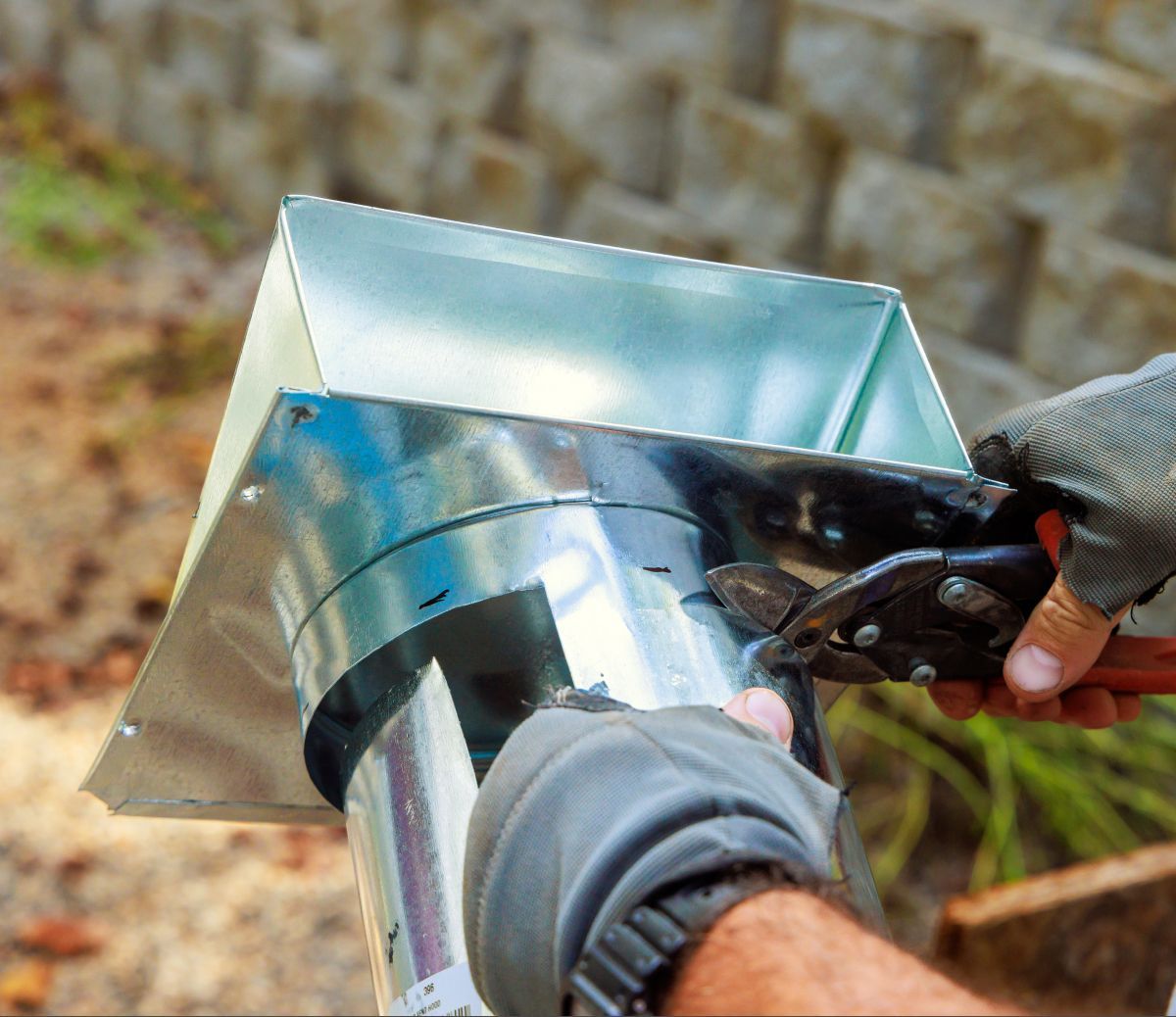 Hands attaching a shiny metal duct to a ventilated box outdoors