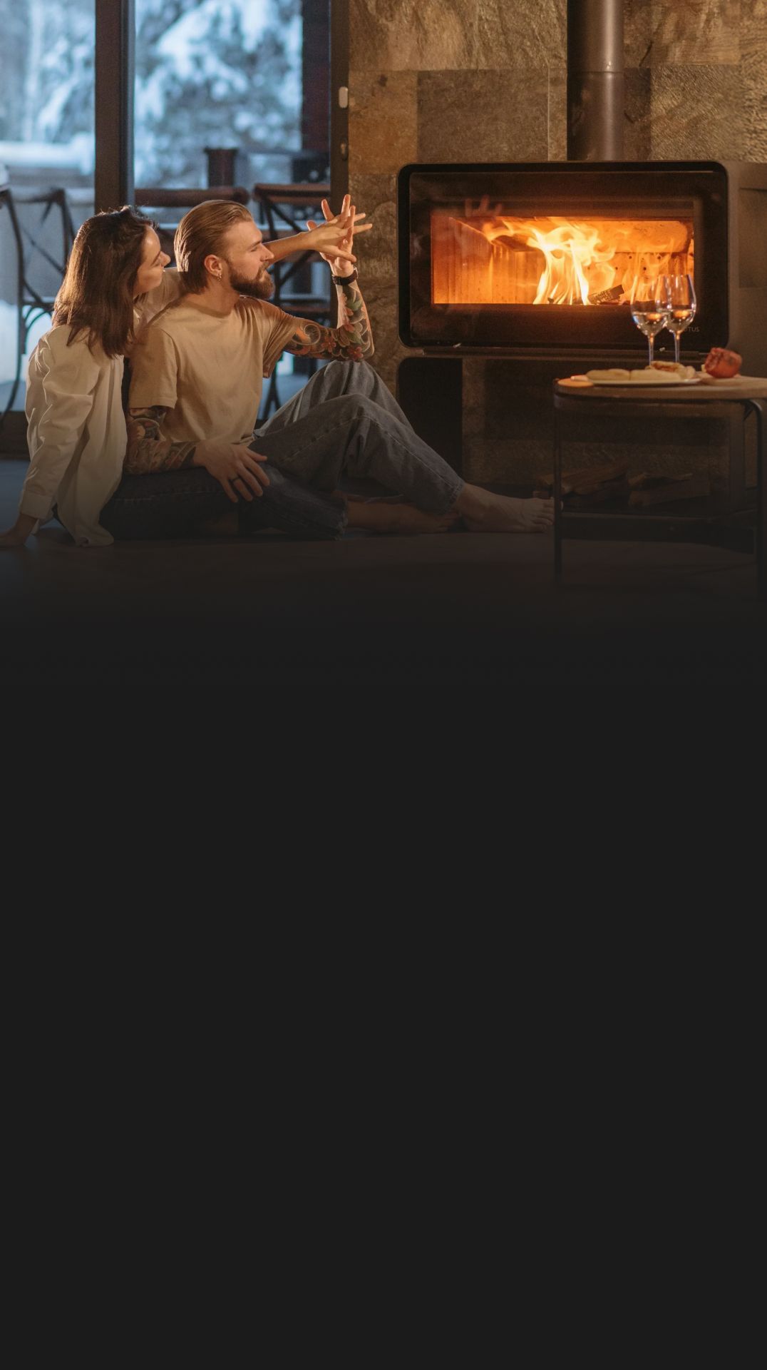 Two people relaxing by a lit fireplace in a cozy living room, one sipping from a mug.