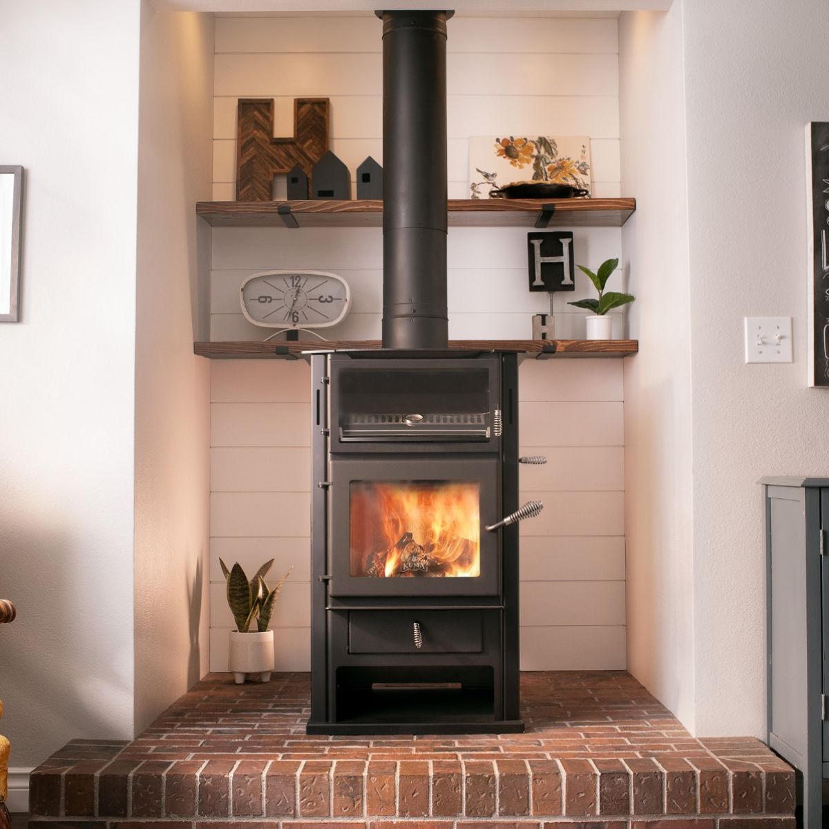 Black wood-burning stove with a fire, set in a white alcove with shelves and brick hearth