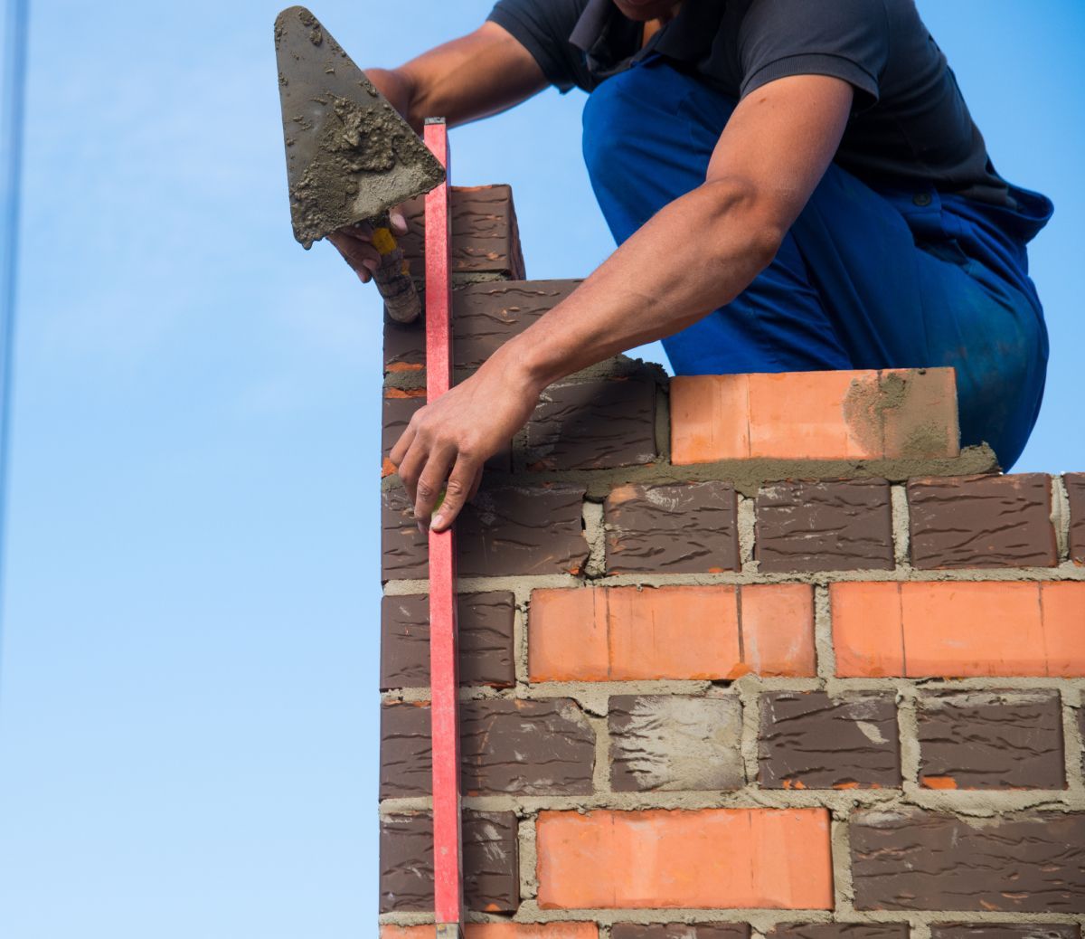 Bricklayer aligning a brick wall with a level against a blue sky