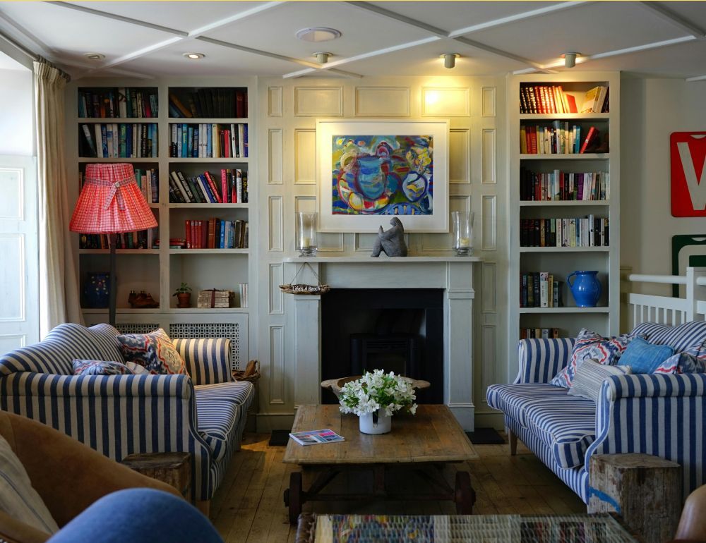 Cozy living room with striped sofas, bookshelves, a fireplace, and a colorful painting above it
