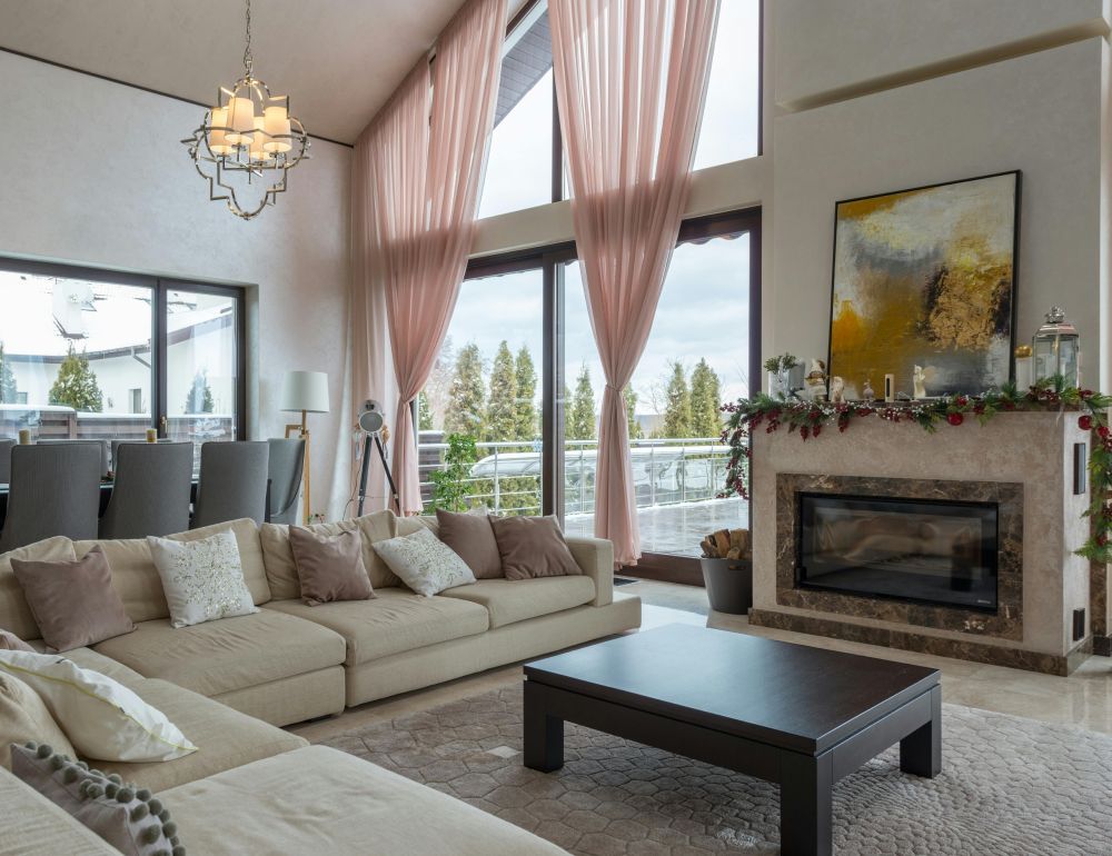 Bright living room with beige sofas, fireplace, coffee table, and tall windows with pink curtains.