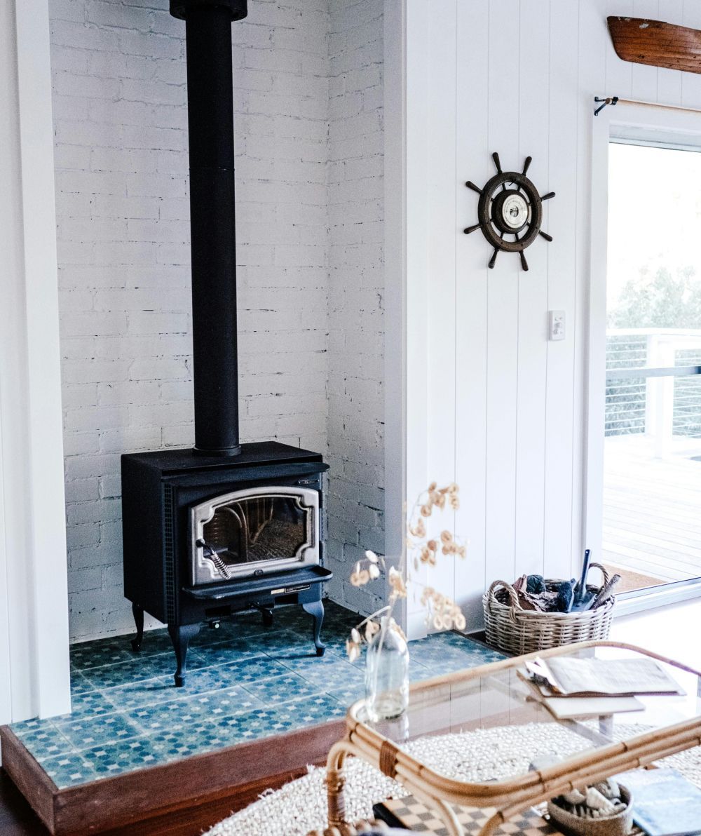 Bright living room with black wood stove, blue-tiled hearth, and sliding glass door to a deck.