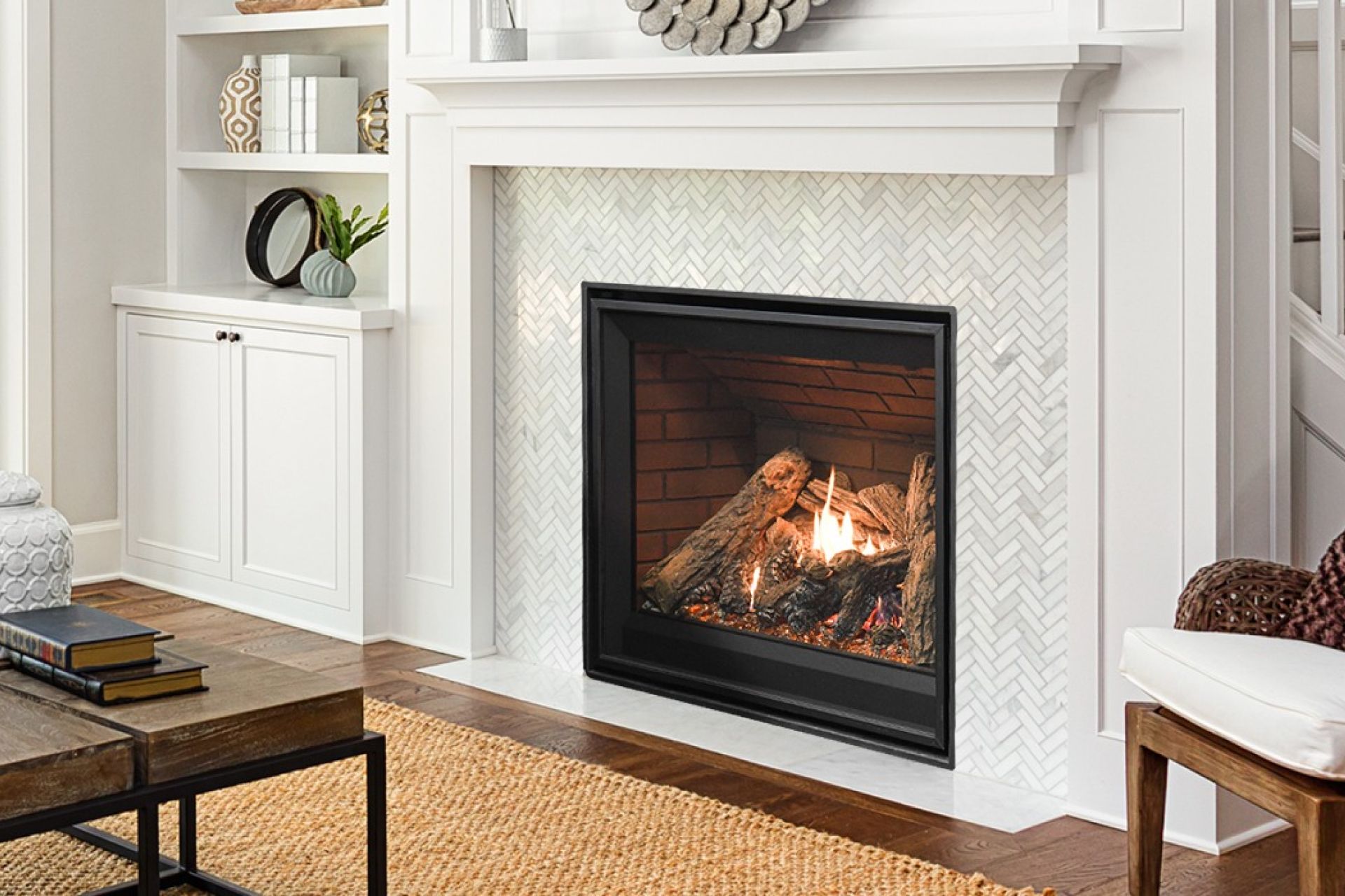 Cozy living room with a black wood stove, glowing fire, and potted plants beside a bright kitchen.