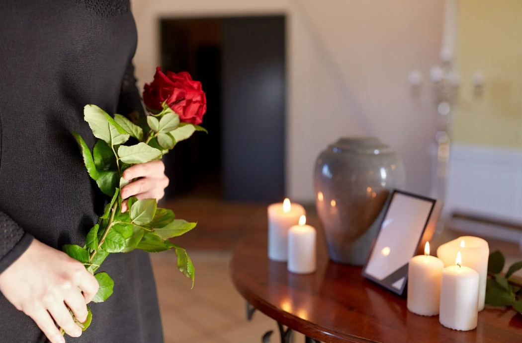 Una persona tiene in mano una rosa rossa accanto a candele accese e una foto incorniciata su un tavolo commemorativo.