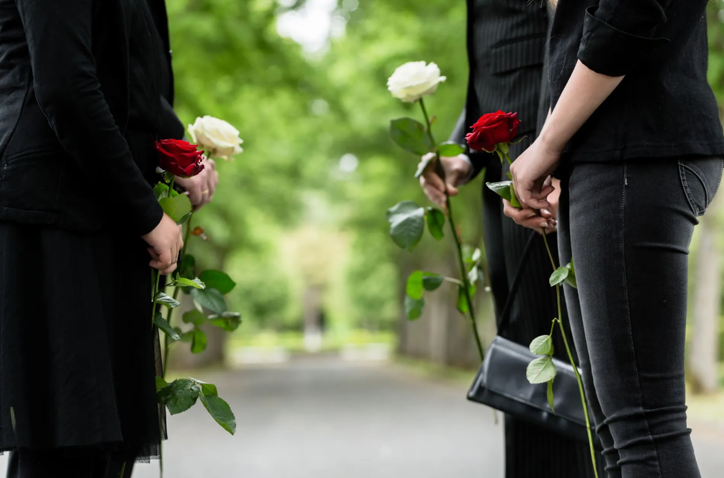 Due persone vestite di nero tengono in mano rose rosse e bianche su un sentiero alberato.