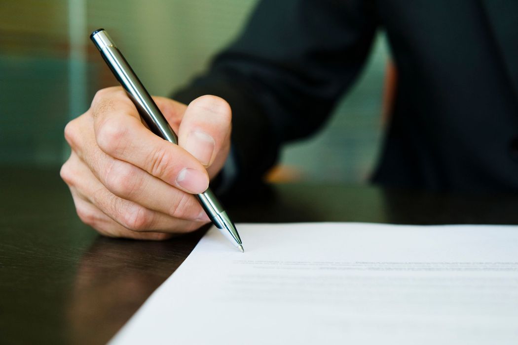 Scrittura a mano su un foglio bianco con una penna argentata a una scrivania