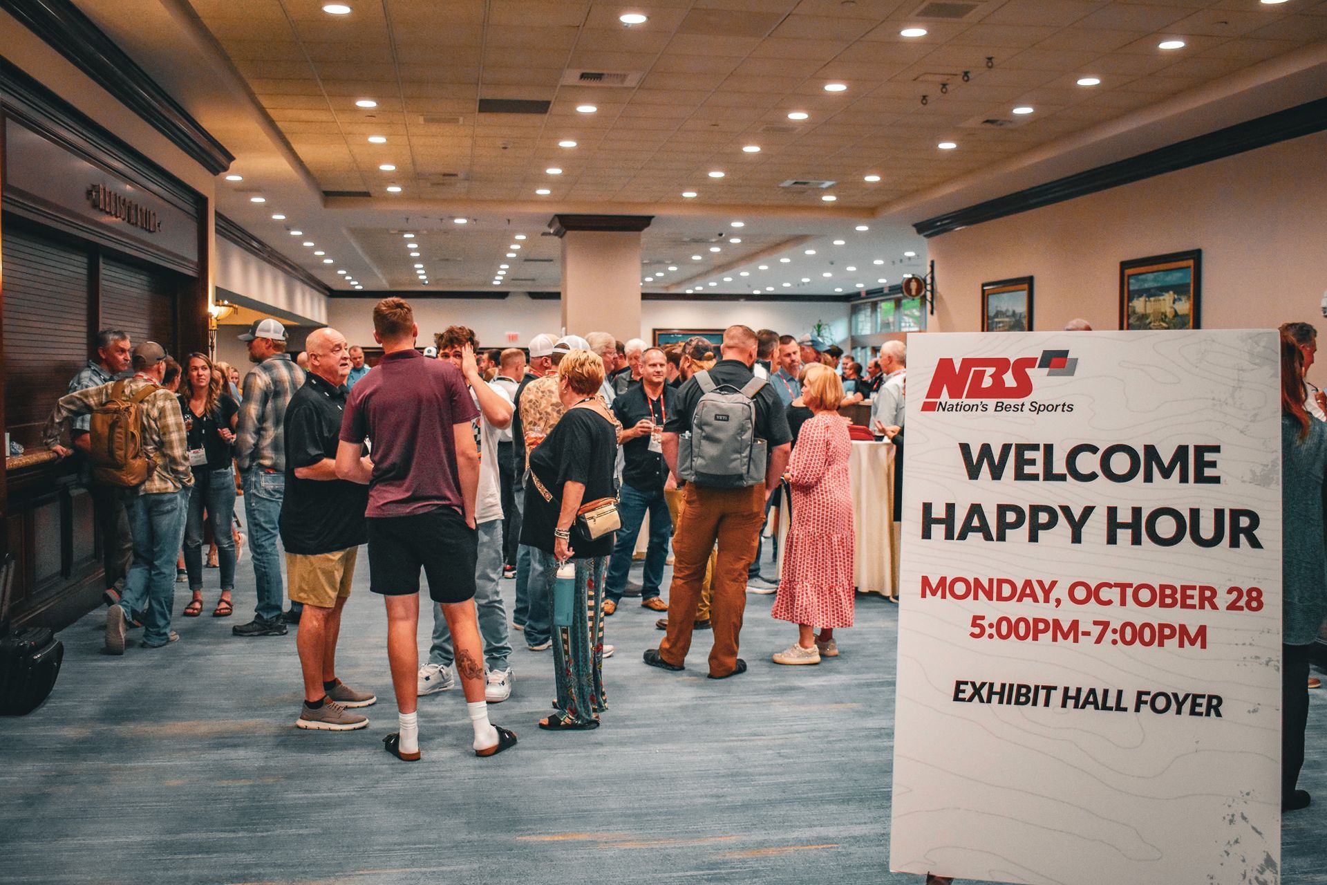 Crowded hotel lobby with a welcome sign for Happy Hour at Embry Hall Foyer