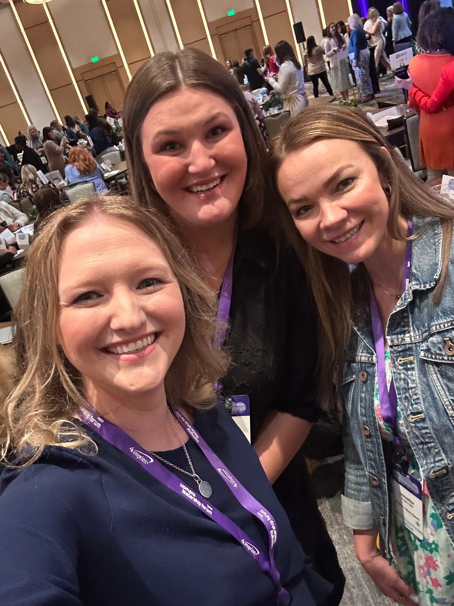 Three smiling people posing together at a conference, wearing lanyards.
