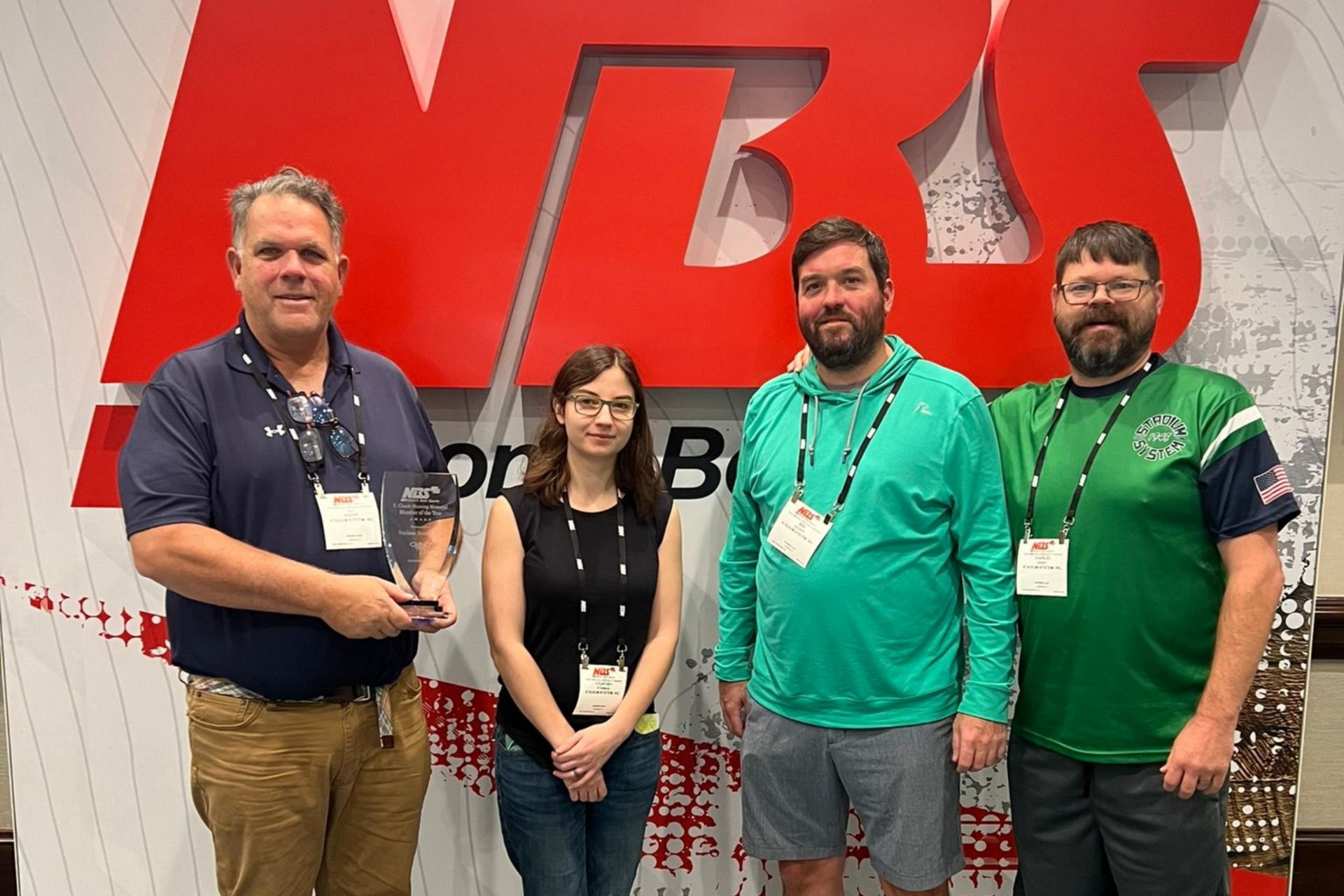 Four people posing at a trade show booth with a large red logo backdrop