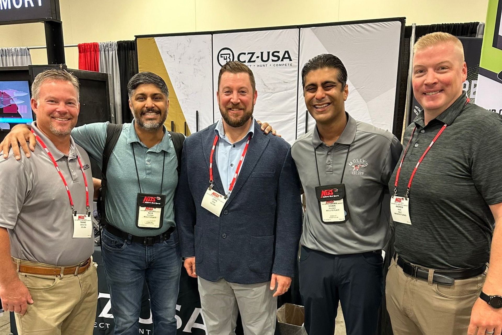 Five men posing at a CZ-USA booth with a branded backdrop at a trade show