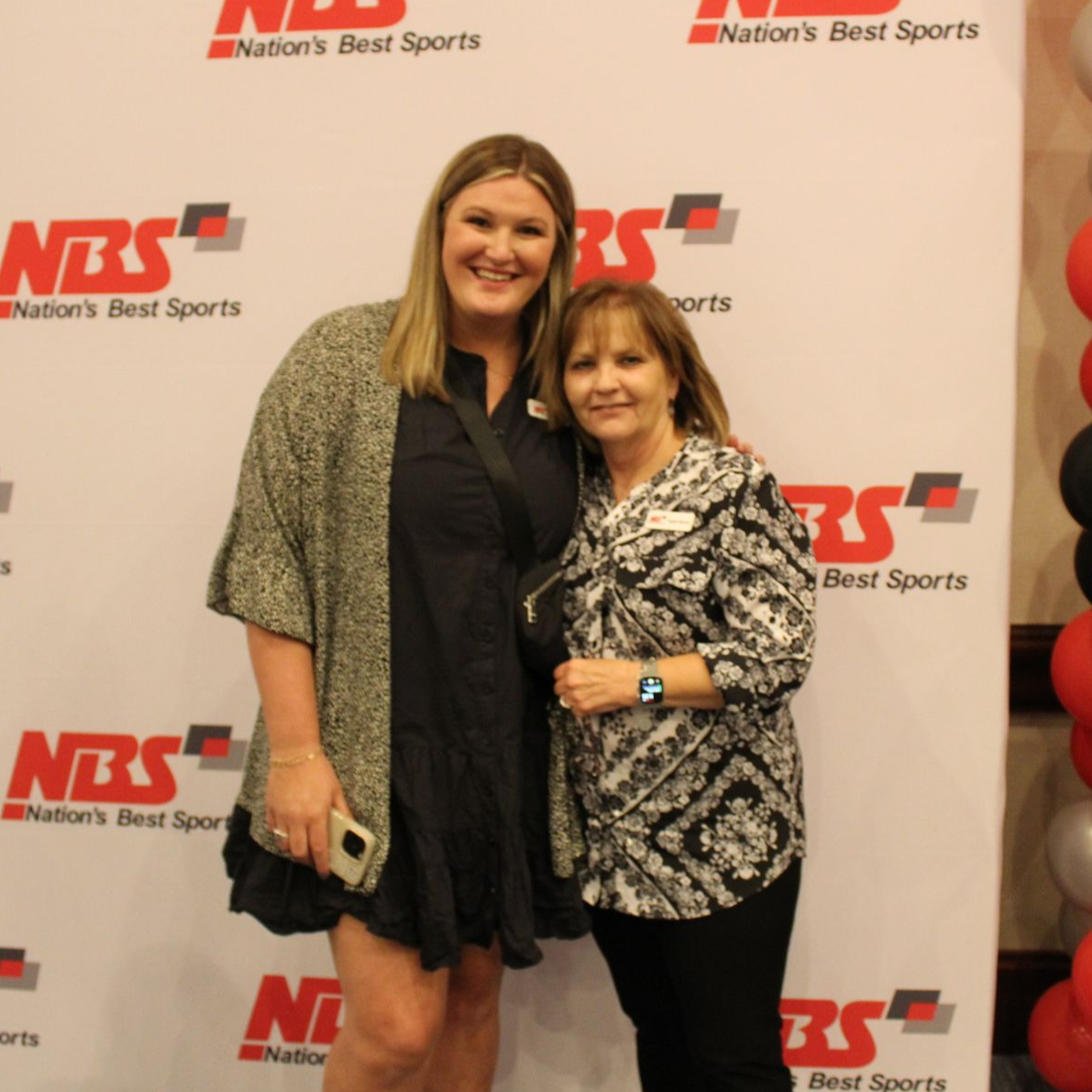 Two women posing and smiling in front of an NBS Nation’s Best Sports backdrop