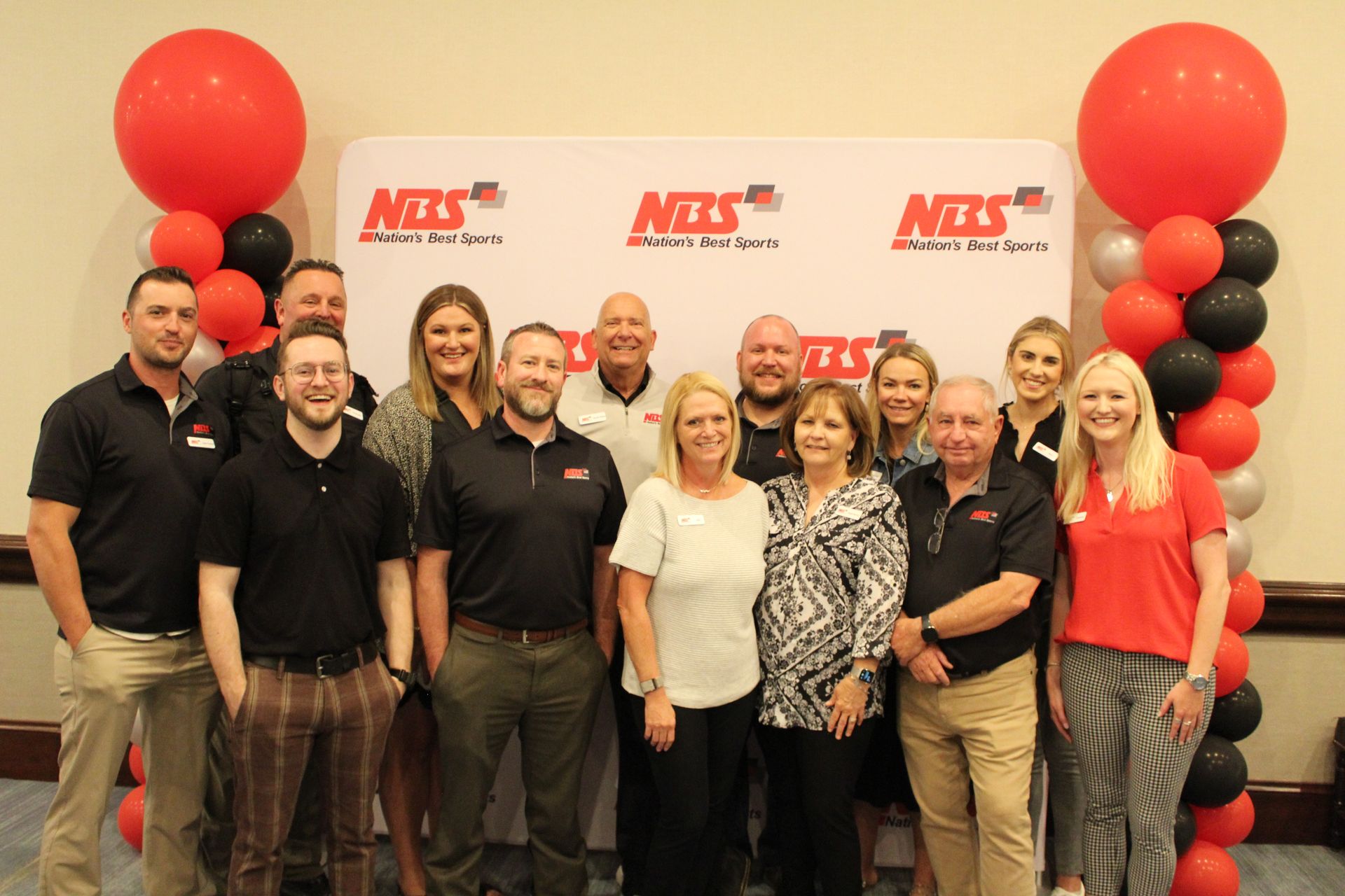 Group of people posing indoors in front of an NBS banner and red-and-black balloon columns