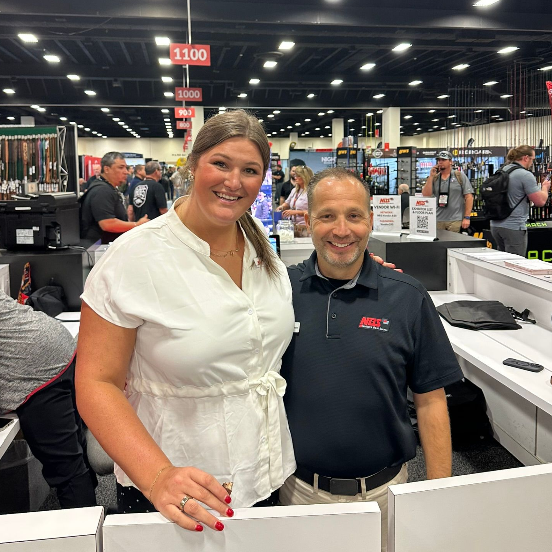 Two smiling people at a trade show booth, standing behind a display counter.