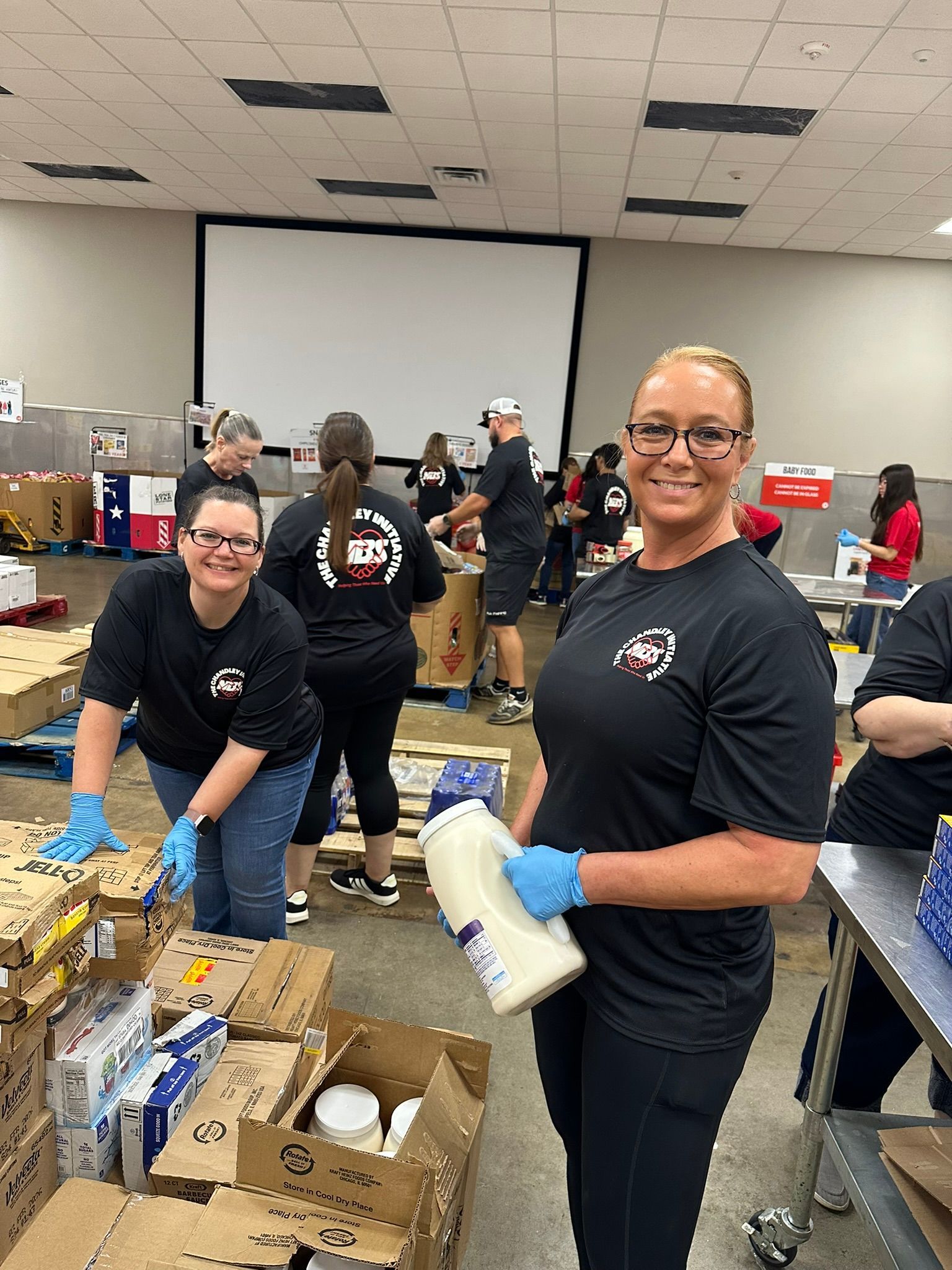 Volunteers packing supplies in a community room, with boxes and tables covered in donated items.