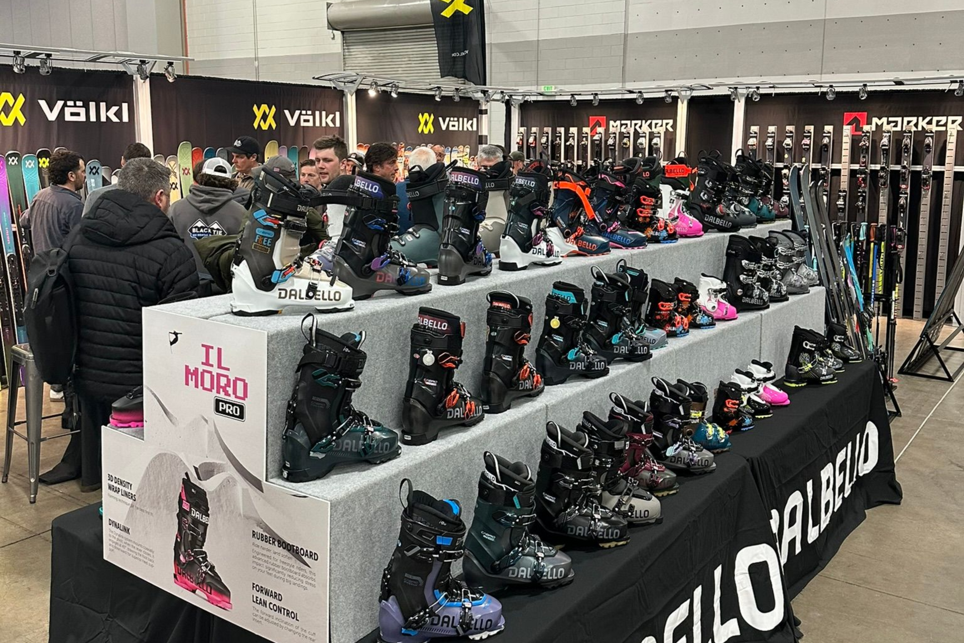 Ski boot display at a busy indoor shop, with rows of black and pink boots on tiered shelves.