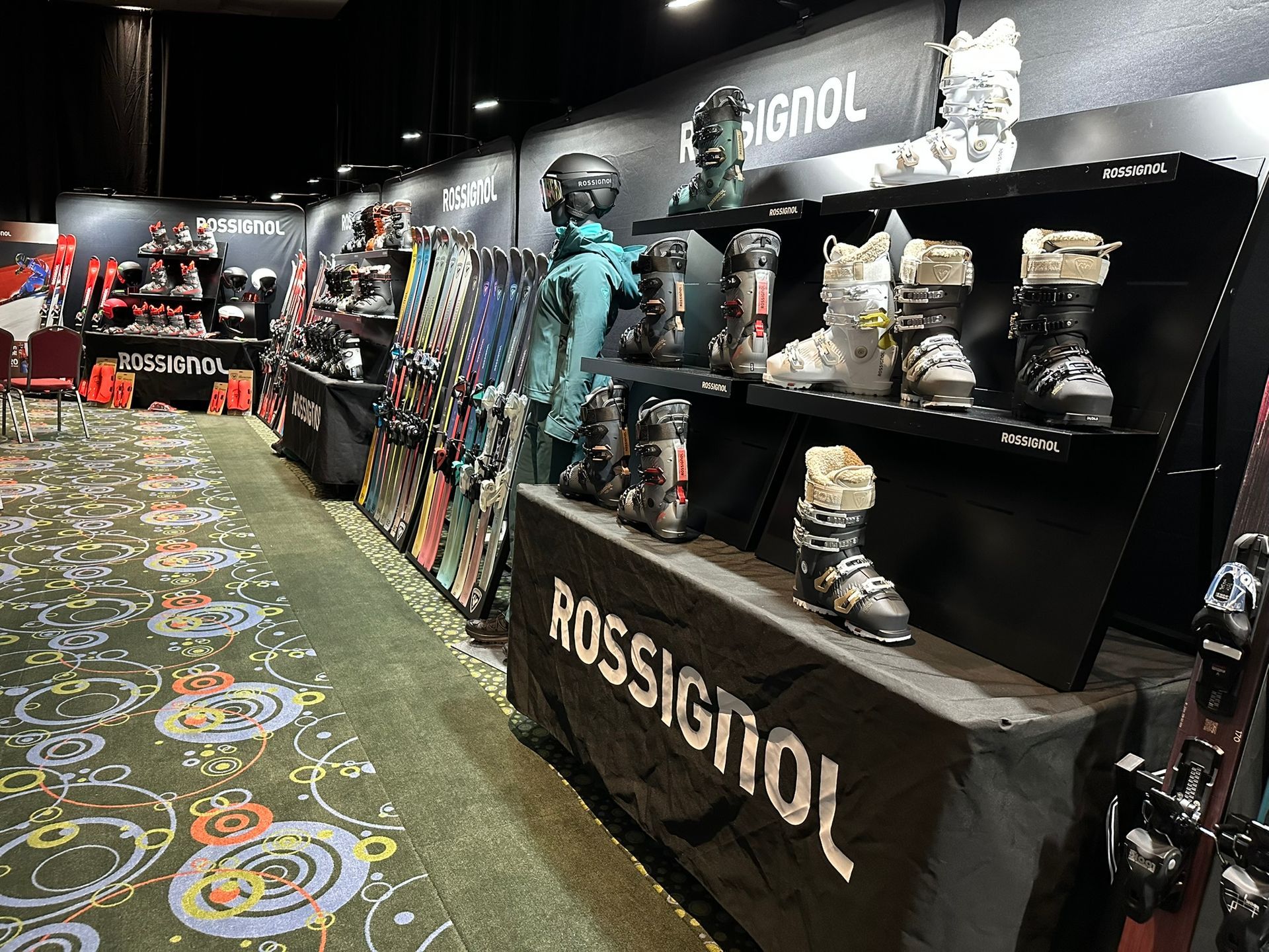 Rossignol ski gear display in a dark retail store aisle with patterned carpet and mannequins in winter clothing