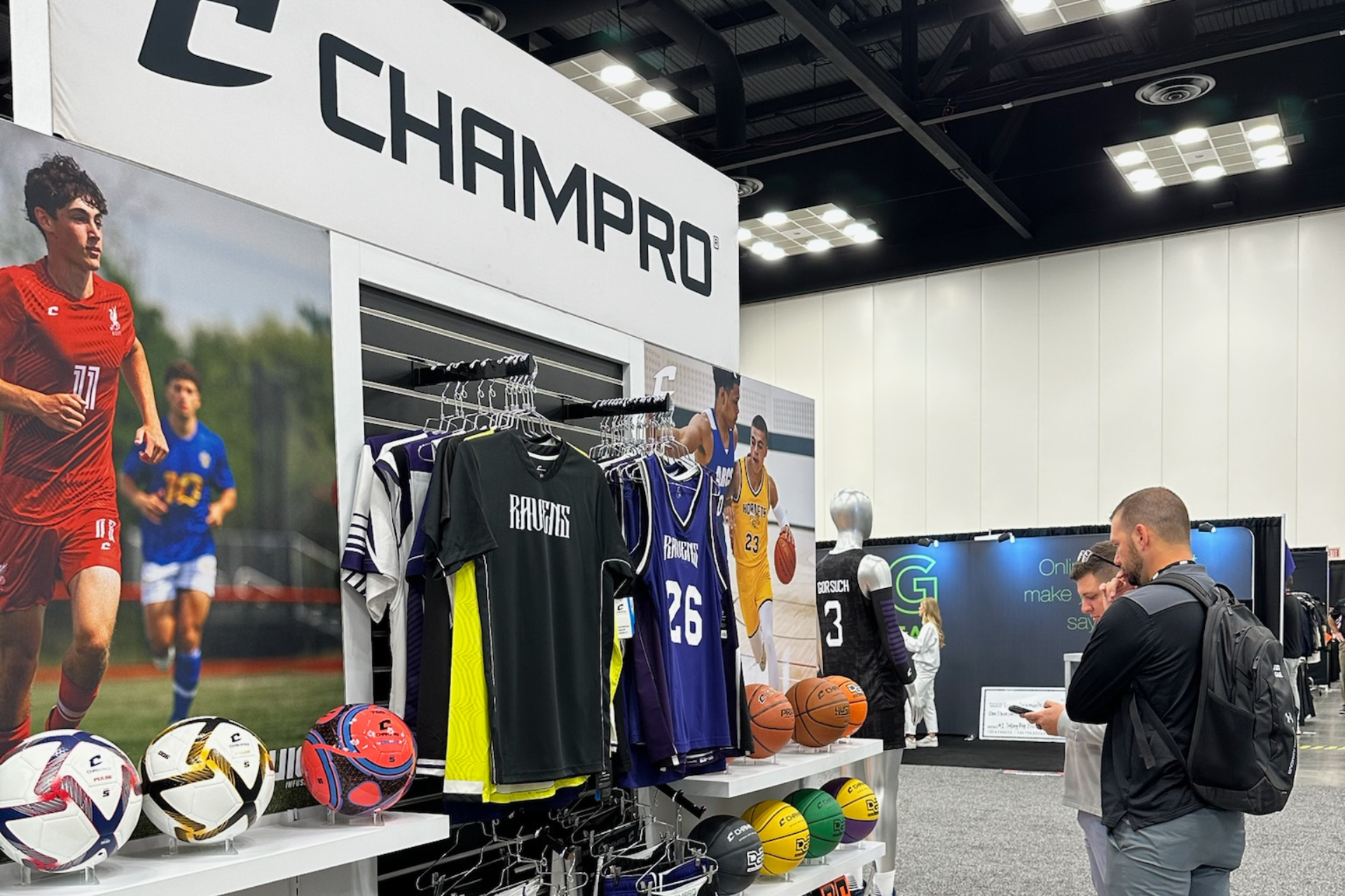 CHAMPRO trade show booth with sports jerseys, soccer gear, and a man browsing displays