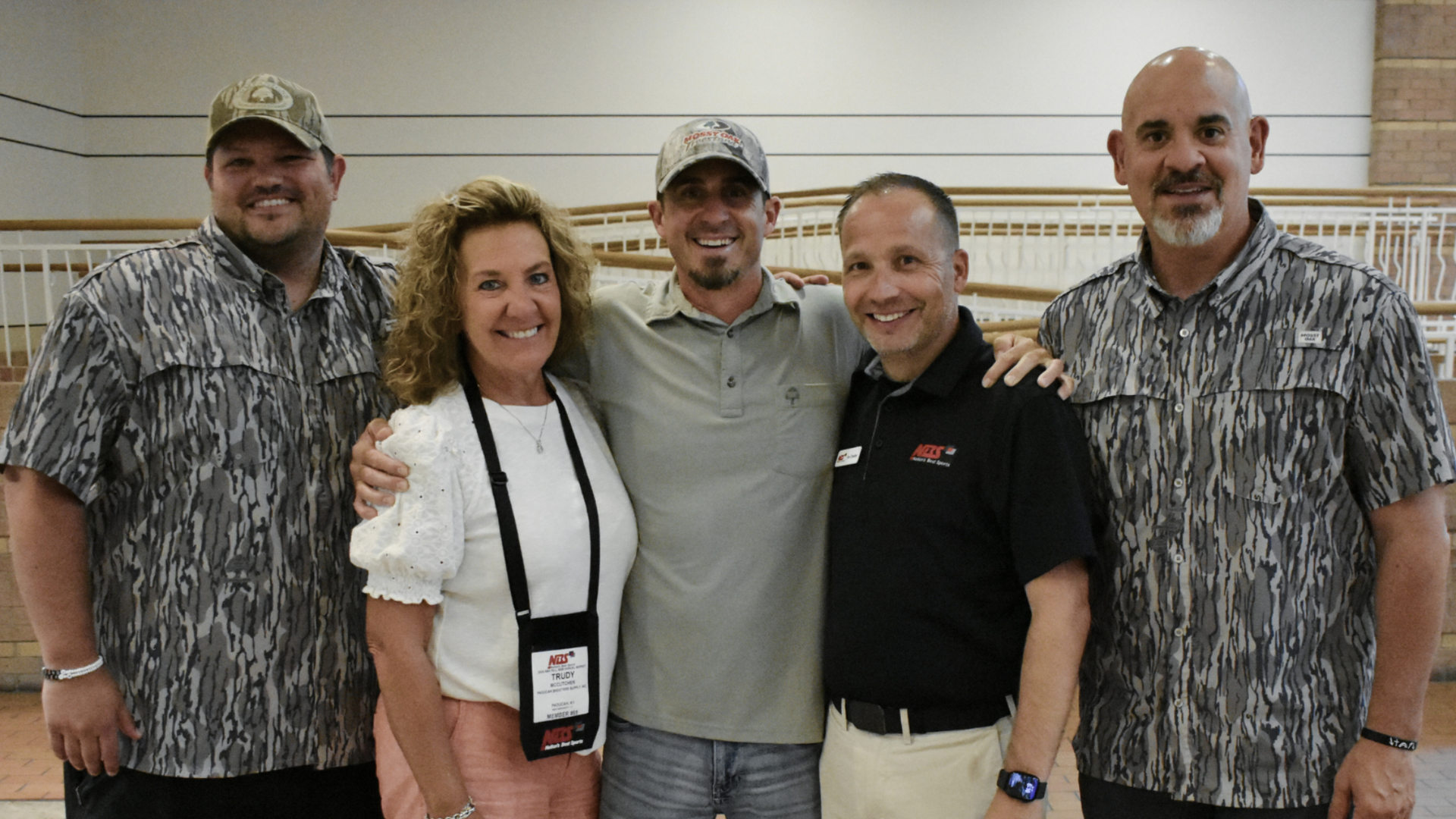 Five people pose indoors, smiling, in casual shirts and lanyards against a striped wall.
