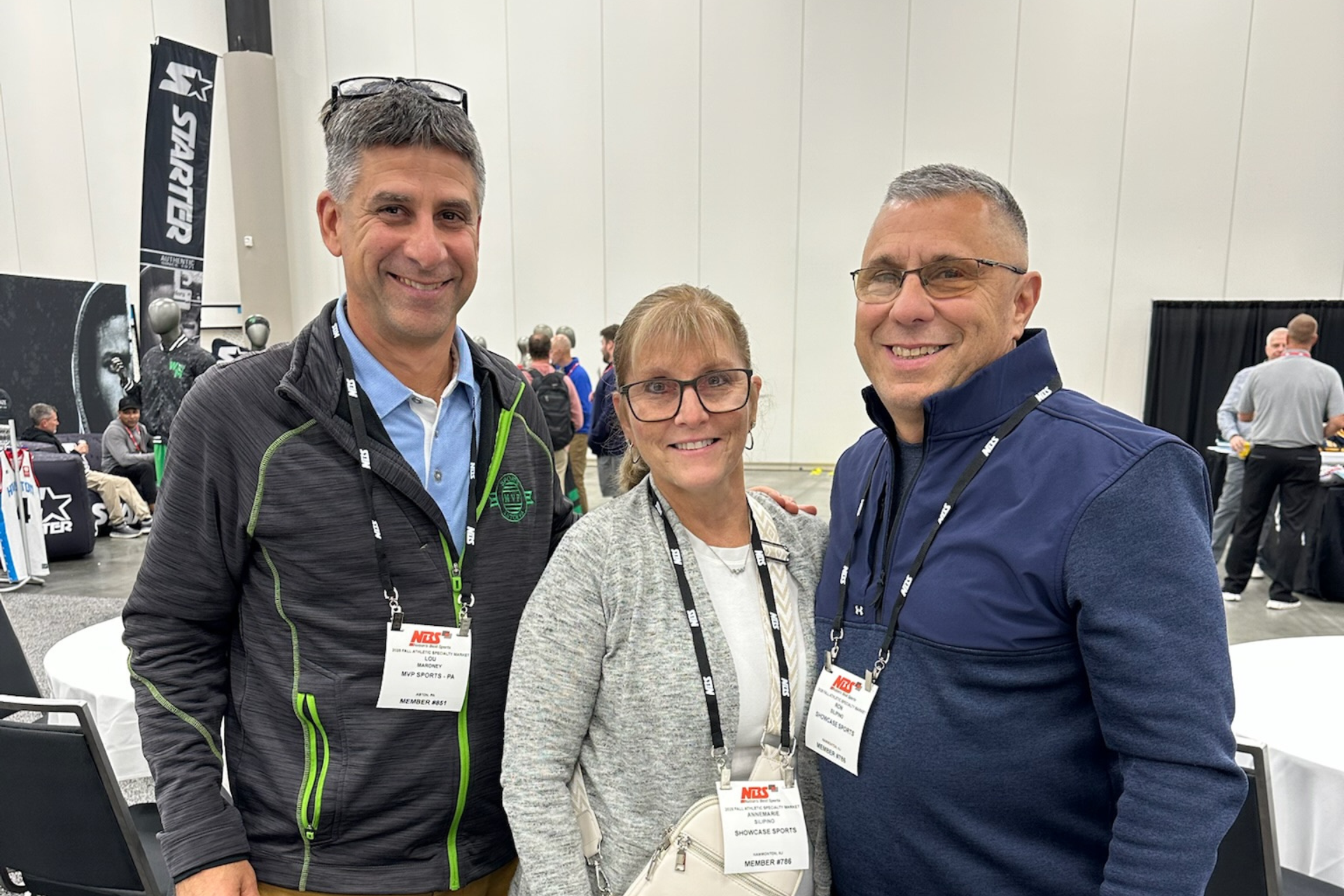 Three people smiling at an indoor event, wearing lanyards and standing together.