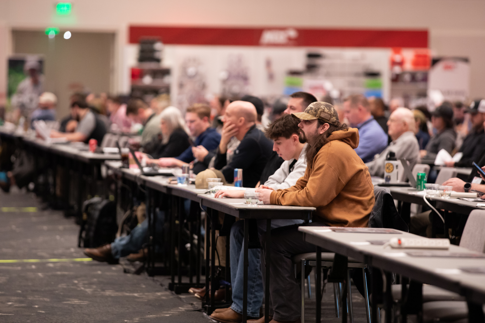 People seated at long tables in a large conference hall, working or listening attentively.