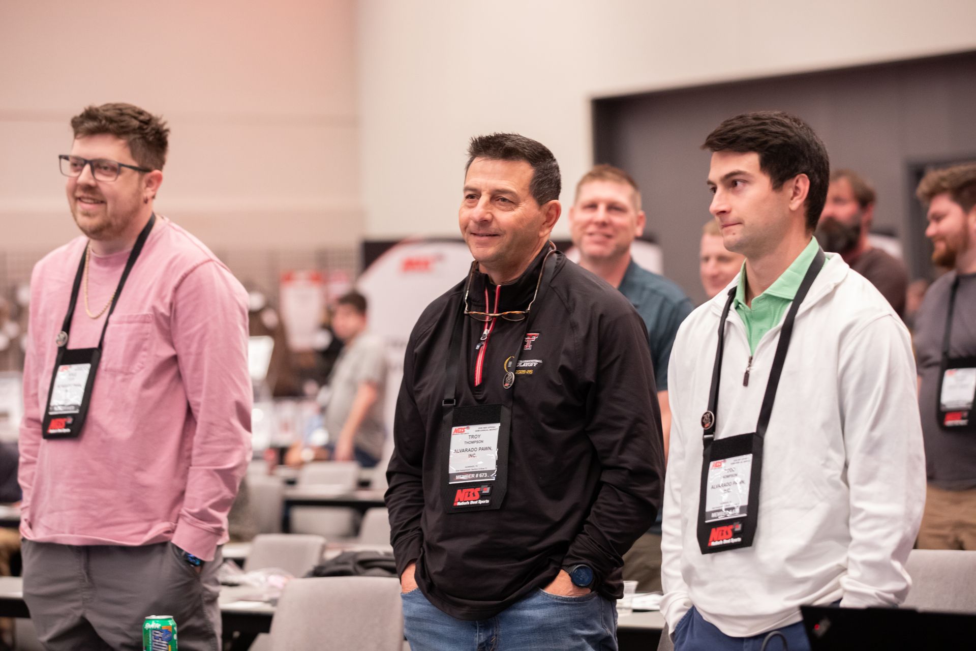Attendees standing at a conference, wearing lanyards and looking toward the stage