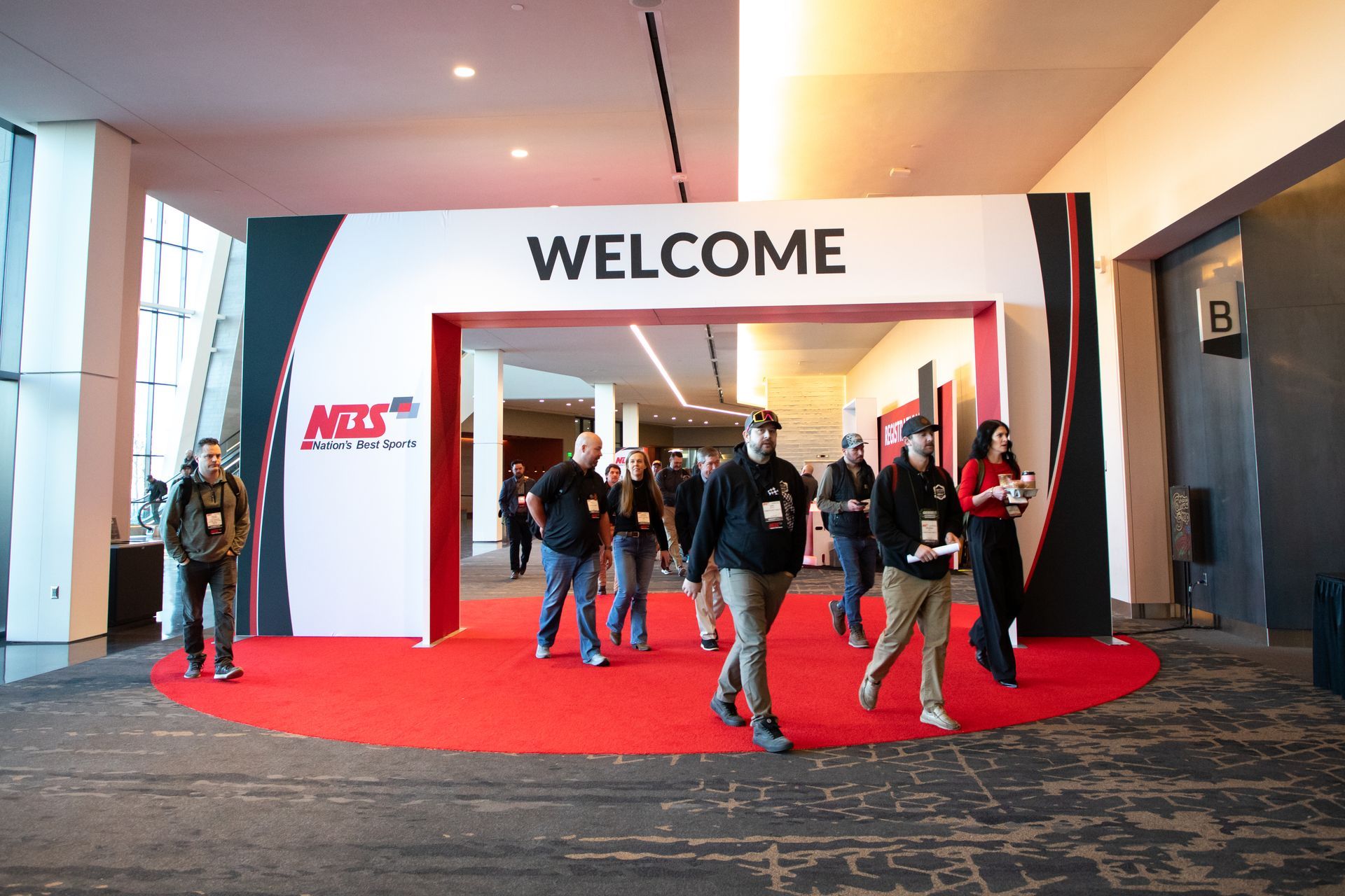 People entering a welcome booth with a red carpet and large “WELCOME” sign