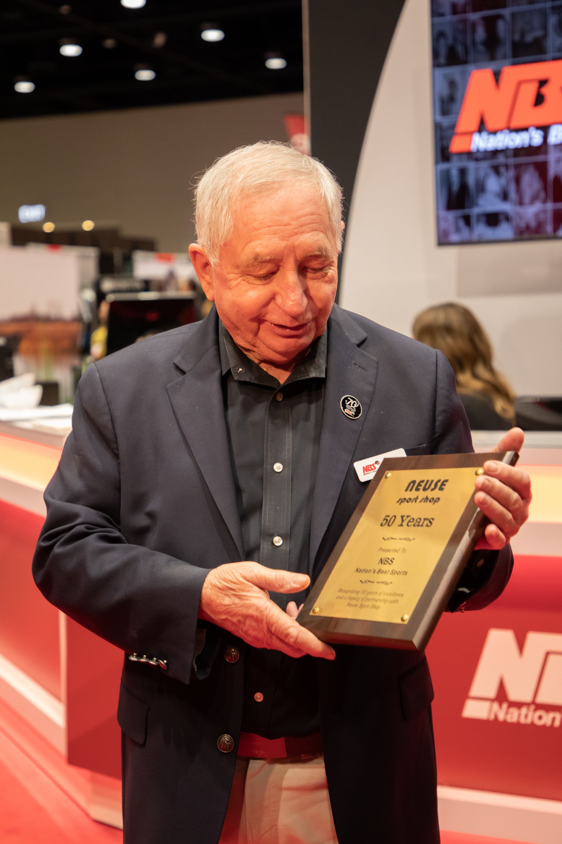 Man holding a framed award at a trade show booth with red and black signage
