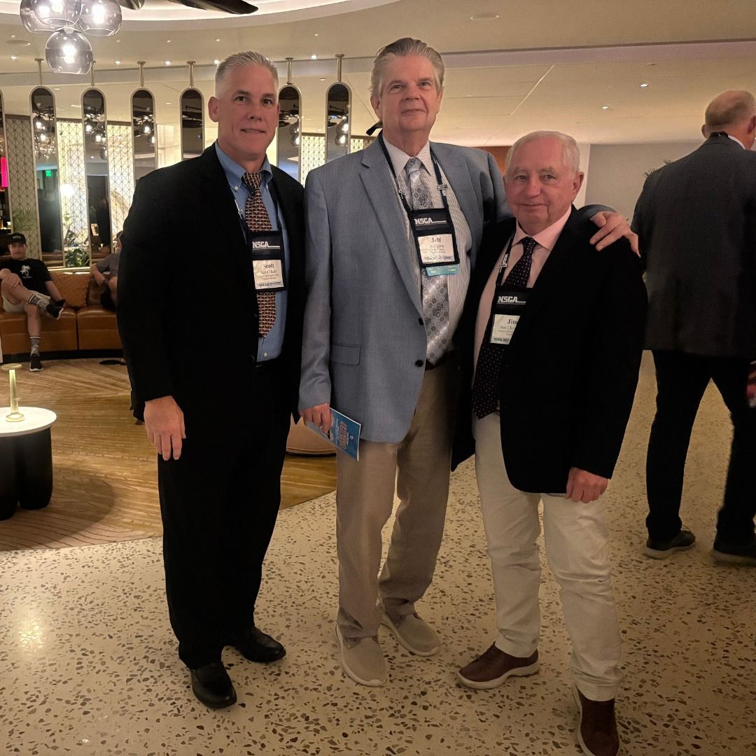 Three men posing together in a hotel lobby, dressed in business attire at a conference.