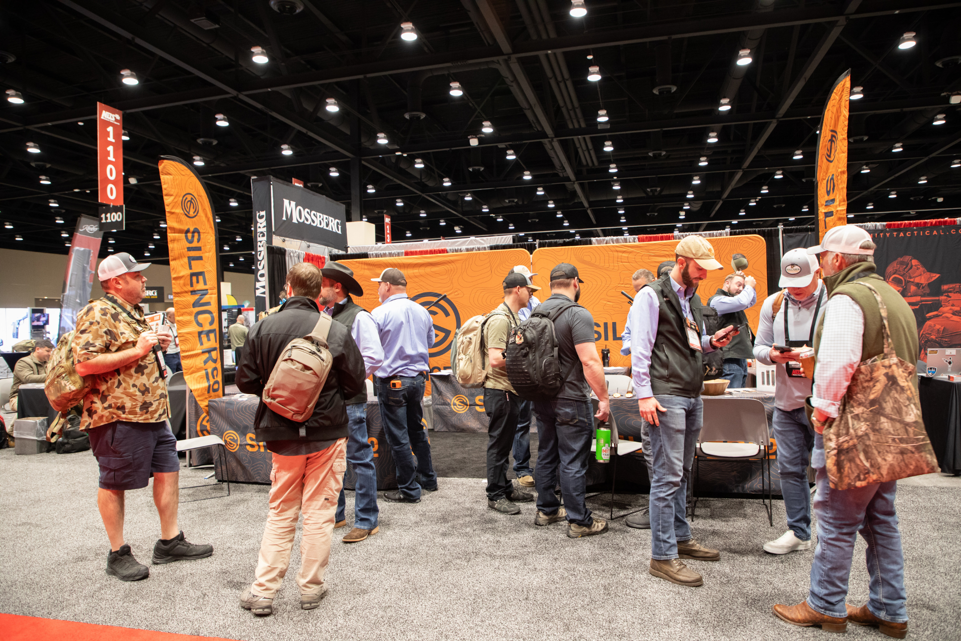 People mingling at an indoor trade show booth with orange banners and an orange-and-black display.
