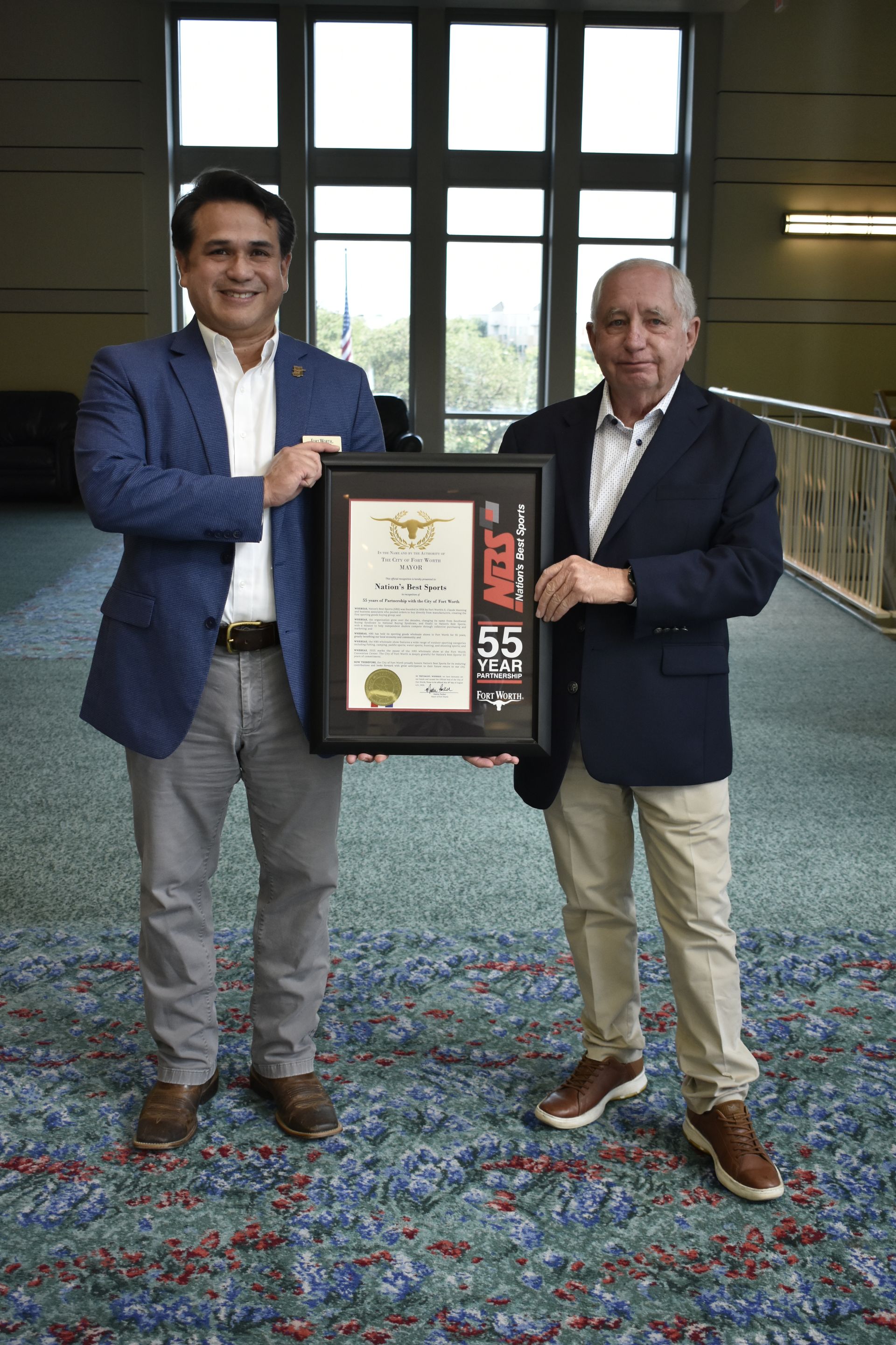 Two men in a hallway hold a framed certificate together.