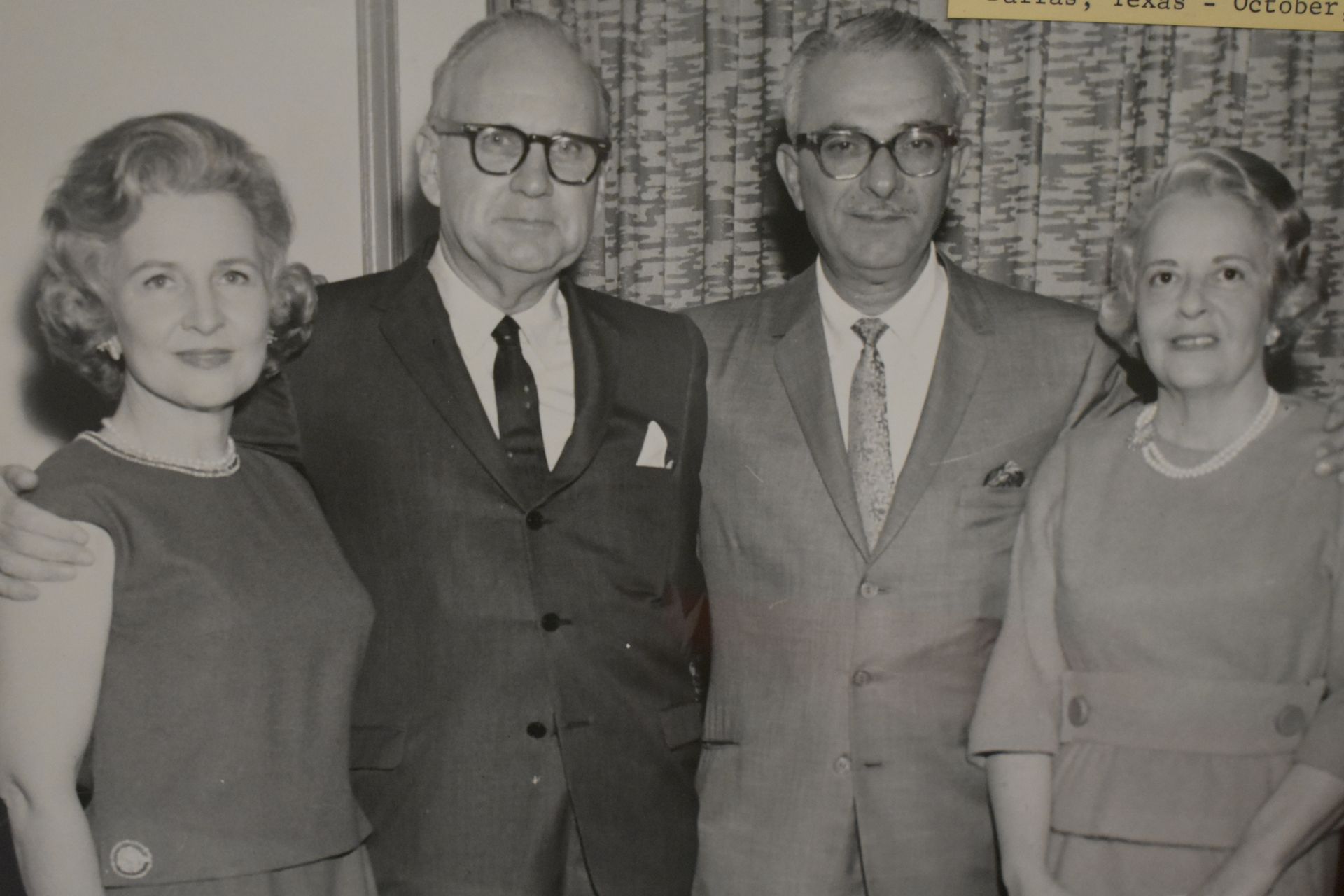 Four people posing in formal attire at an indoor event, standing in front of patterned curtains.
