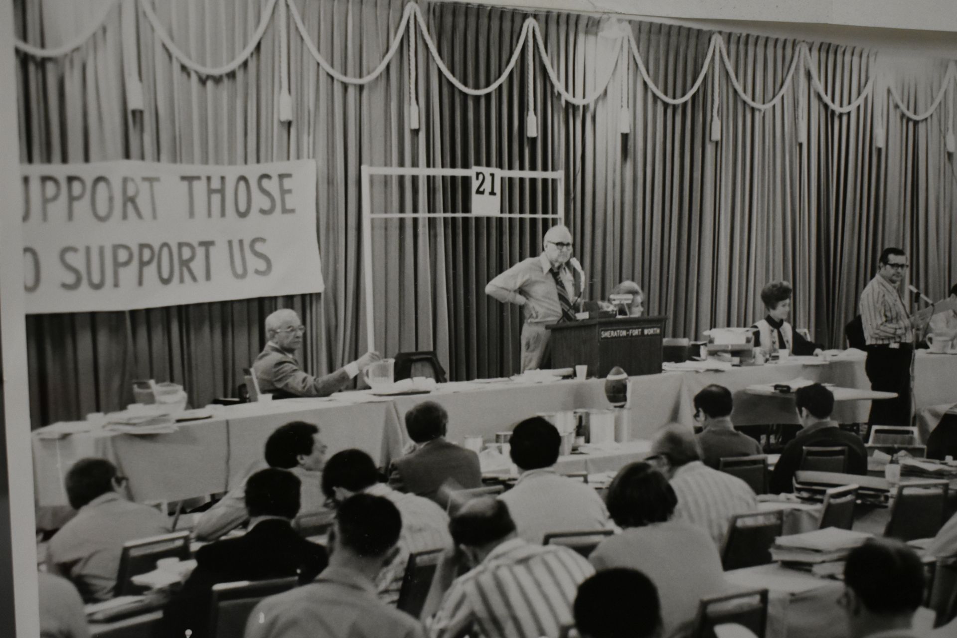 Panel discussion in a crowded auditorium, with speakers at a long table and a banner in the background.