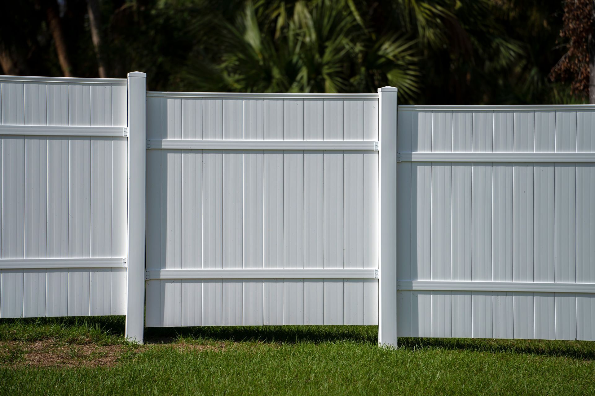 White vinyl privacy fence panels installed along a grassy yard with trees in the background.