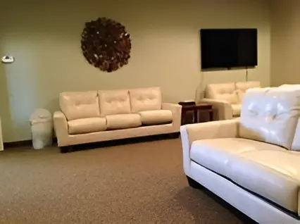 Empty living room with beige sofas, a black TV, and a decorative wall wreath on tan carpet.