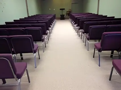 Empty room with rows of purple chairs facing a front podium