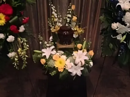 Floral funeral altar with white, yellow, and pink flowers around a central urn
