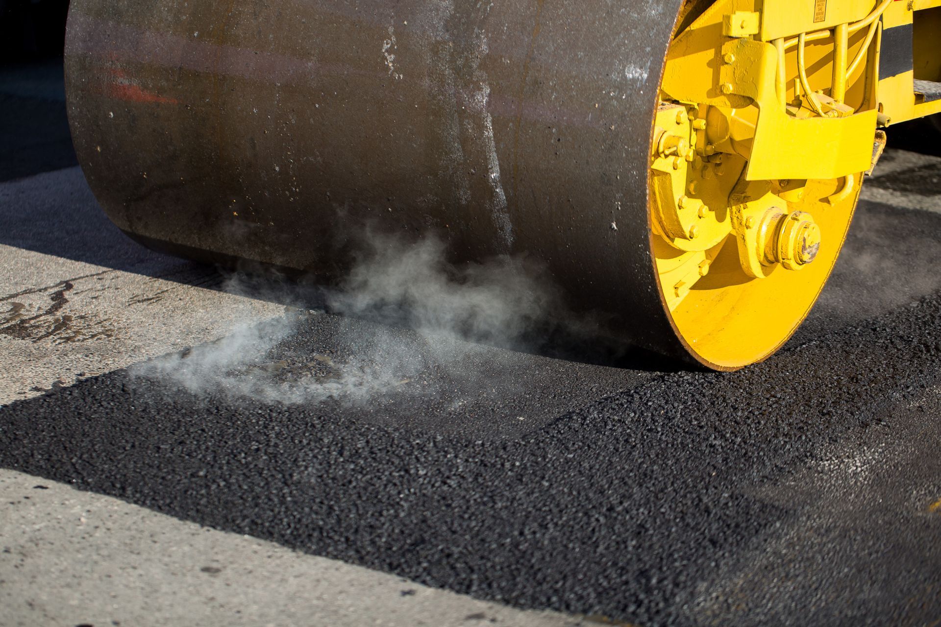Steam rising as a road roller compacts hot asphalt during paving work.
